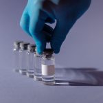 Profissional de saúde usando luvas manipula frascos de vacina em um ambiente estéril.