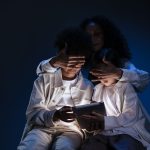 Mãe acompanha duas crianças que utilizam um tablet, representando supervisão e segurança no uso de mídias digitais.